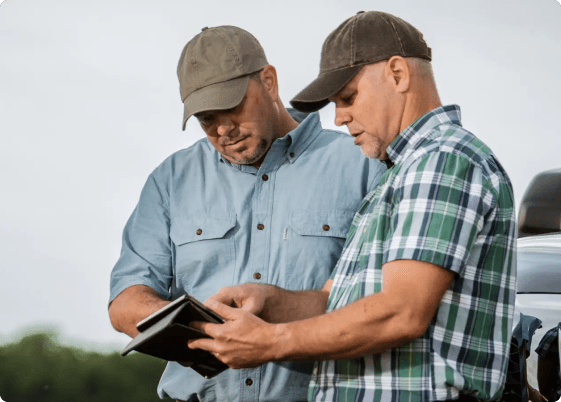 Two men look at a notebook while in a field